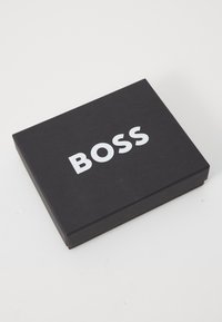 Juodas stačiakampis dėžė su lygiu paviršiumi, viršuje esantis drąsus baltas užrašas "BOSS". Paprastas ir minimalistiškas dizainas.