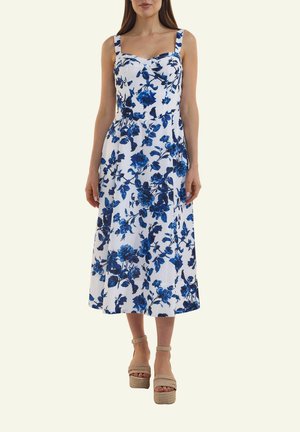 Weißes ärmelloses Midikleid mit blauem Blumenmuster, quadratischem Ausschnitt, tailliertem Oberteil und ausgestelltem Rock, kombiniert mit beigen Plateau-Sandalen.