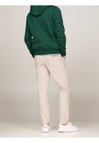 Zelená mikina s kapucí, světlé béžové kalhoty a bílé tenisky. Ležérní oblečení s volným střihem a texturovaným povrchem mikiny.