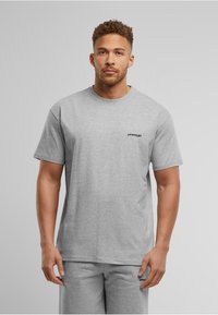 Graues T-Shirt mit kurzen Ärmeln aus Baumwollmischung und rundem Halsausschnitt, mit einem kleinen schwarzen "UPGRADE"-Logo auf der linken Seite.