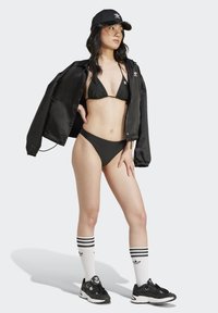 Černé bikini s trojúhelníkovým vrškem a nízkými kalhotkami, doplněné černou bomber bundou, černou čepicí a černými teniskami se bílými pruhy.