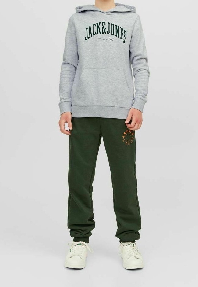 Felpa grigia con "JACK&JONES" in testo verde, abbinata a pantaloni della tuta verde scuro con un logo arancione. Sneakers bianche completano l'outfit.