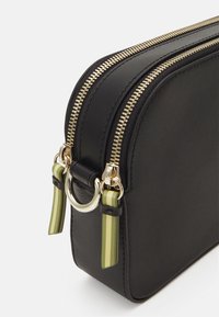 Borsa in pelle nera di forma arrotondata, con doppie cerniere dorate, accessori in oro e dettagli a strisce verdi attaccati ai cursori delle cerniere.