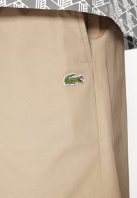 Beige shorts med en slät yta, med en broderad grön krokodil-logotyp framtill och subtila sidofickor.