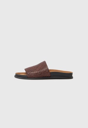 Brown woven slide sandal with a textured woven upper, flat black sole, and cushioned footbed. Designed for casual wear.