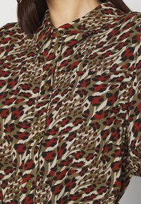 Camicia con bottoni realizzata in tessuto leggero, caratterizzata da una stampa di animali astratta nei colori rosso, nero e verde, con una texture morbida e un colletto classico.