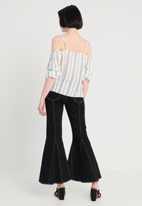 Top bianco off-the-shoulder con strisce nere verticali, abbinato a jeans neri a palazzo con cuciture bianche e una texture liscia.