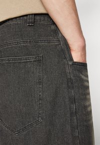 Falda de mezclilla gris oscuro con un bolsillo trasero, sutil desgaste y una textura suave. Costuras visibles y un detalle de botón en la cintura.