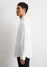 Witte lange mouwen overhemd met een knoopsluiting en een losse pasvorm. Glad katoenen stof, rechte zoom en manchet met knopen. Draagt met donkere broek.