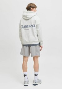 Szara bluza z kapturem ma duże logo "AERO" i miękką teksturę. Połączona z jasnoszarymi szortami, białymi skarpetkami i szarymi butami sportowymi, na neutralnym tle.