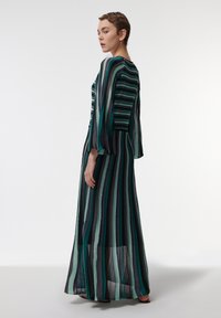Robe maxi en tissu transparent avec des rayures verticales en teal, noir et vert. Manches longues à coupe ample et silhouette fluide.