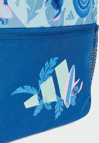 Mochila azul con un tejido texturizado, gráficos de hojas de palmera y un pequeño personaje sosteniendo una tabla de surf. Los detalles de diseño notables incluyen formas en capas.