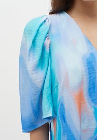Blauw en koraal abstract patroon top met opgestoken korte mouwen, voorzien van een V-hals en zachte, lichte stof. Randen zijn licht rauw.