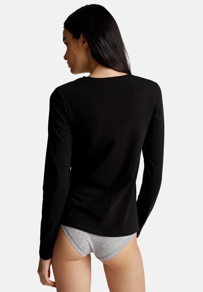Schwarzes Langarmhemd aus glattem Stoff, mit einfachem Rundhalsausschnitt und taillierter Silhouette. Getragen mit grauer Unterwäsche.