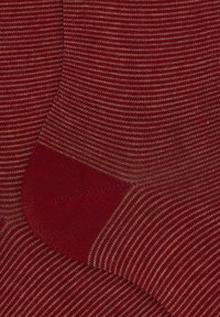 Calzini a righe rosse e beige presentano una texture a coste e sezioni di tallone e punta solidi rossi. Il tessuto sembra morbido ed elastico.