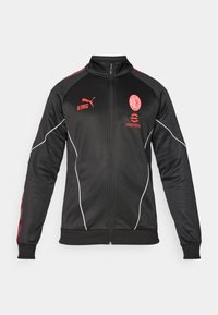 Sort sportsjakke med røde accenter, lynlås, høj krave, Puma-logo og holdmærke. Har tekstureret stof og hvide piping-detaljer.