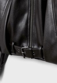 Giacca nera in pelle con dettaglio cerniera e texture liscia. Presenta una cintura con accessori metallici e un design aderente.