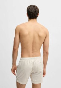 Herren Badeshorts in hellem Beige mit geometrischem Muster. Sie verfügen über einen elastischen Bund, Seitentaschen und genähte Details.