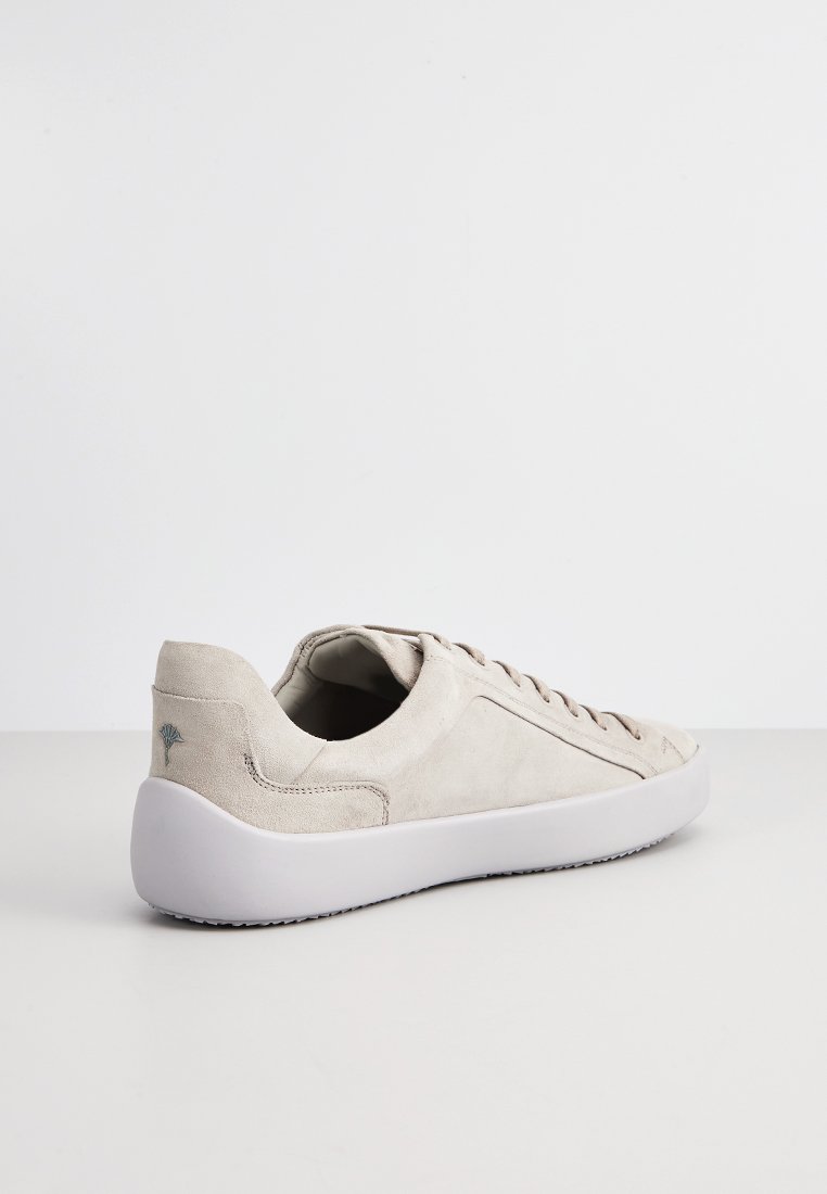 Beżowe zamszowe sneakersy z białą gumową podeszwą, z zawiązywaną konstrukcją i subtelnym akcentem logo na pięcie. Gładka tekstura na całej powierzchni.