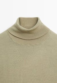 Olivgrön polotröja med ribbad textur, med en lagerdesign vid nacken och slät tyg. Perfekt för lagerläggning.