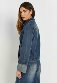 Jeansjacka i mörk tvätt med långa ärmar och en klassisk krage. Har kontrasterande ljusa denim manschetter och en strukturerad passform.