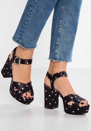 Mustat korolliset avokkaat, joissa on valkoisia pilkkuja, käytetty revityn sinisten farkkujen kanssa. Varpaat näkyvissä ja kynnet lakattu mustalla kynsilakalla.