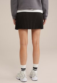 Faltender schwarzer Rock aus strukturiertem Stoff, kombiniert mit schwarz-weißen gestreiften Socken und hellen Turnschuhen.