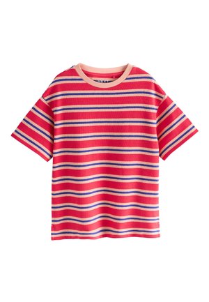 Kind trägt ein rot gestreiftes Shirt und blaue Jeans, hält eine Jeansjacke und steht auf einem braun-weiß karierten Boden.