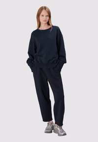 Navyblauwe sweatshirt en bijpassende joggingbroek van zachte stof met een losse pasvorm. Zilveren sneakers maken de outfit compleet. Eenvoudig, minimalistisch ontwerp.