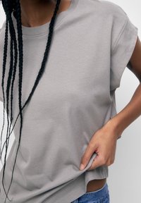 Grå crew-neck t-shirt lavet af blødt stof, med korte ærmer og en afslappet pasform. Lidt længere bagpå med en glat tekstur.