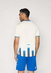 Witte sporttrui met een gestructureerd oppervlak, blauwe accenten en een gradiëntontwerp met verticale zwarte en blauwe strepen. Blauwe shorts.