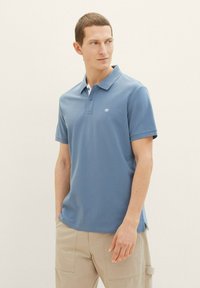 Kurzärmeliges Poloshirt in Hellblau mit klassischem Kragen, Knopfleiste und kleinem Logo auf der Brust. Glatte Stoffstruktur.