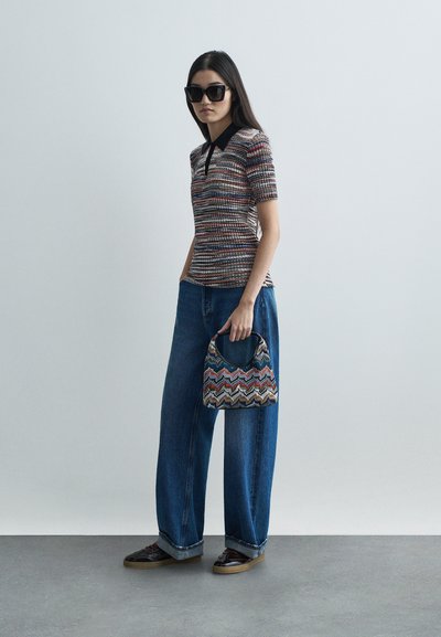 Pleteni polo majica s kratkim rukavima i crnim ovratnikom, u kombinaciji s širokim plavim trapericama i torbom s multikolornim cik-cak uzorkom. Crne sunčane naočale.