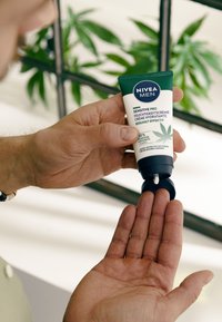 NIVEA Men Sensitive Pro cream in a green squeeze tube, being dispensed onto a hand. Tube features white accents and leaf graphic.