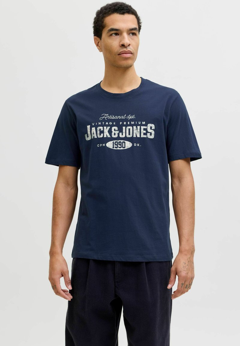 Camiseta de algodón azul marino de mangas cortas. Presenta un gráfico vintage en blanco con "Jack & Jones" y "Copenhague 1990."