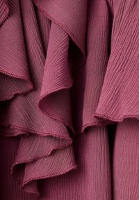 Gros plan d'un tissu texturé et froncé de couleur mauve profond avec des plis superposés et des bords délicatement finis.