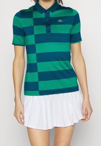 Green and navy striped polo shirt with a collar and three buttons, paired with a white pleated skirt. Lacoste logo on the left chest.