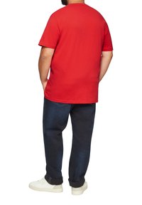 Rode katoenen t-shirt met korte mouwen, relaxte pasvorm, ronde hals, gecombineerd met donkerblauwe jeans en witte sneakers.