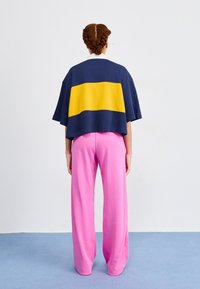 Marineblauwe en gele kleurblok oversized t-shirt gecombineerd met losse, roze wijde broek, beide gemaakt van zachte, ademende stof.