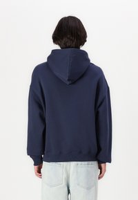 Felpa con cappuccio blu navy, dal taglio rilassato, con polsini e bordo a coste. Tessuto liscio, senza motivi o dettagli visibili.