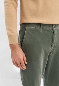 Zielone sztruksowe spodnie o prążkowanej fakturze, z przednimi kieszeniami i zapięciem na guziki. Połączone z beżowym, dzianym swetrem.