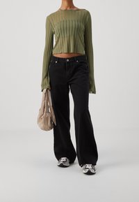 Hellgrünes, geripptes Langarm-Crop-Top, hochtaillierte schwarze Schlagjeans, beiger Beutel und sportliche schwarze Schuhe mit weißen Akzenten.