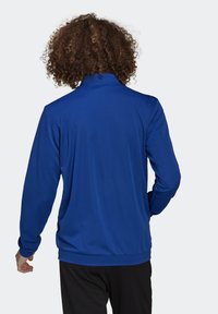 Blå sportjacka med långa ärmar, hög krage, slät yta och avslappnad passform. Inga synliga mönster eller detaljer i metall.