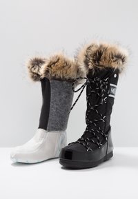 Botte d'hiver noire avec bordure en fourrure et lacets, à côté d'une doublure de botte isolante amovible grise et blanche sur fond blanc.