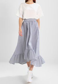 Paski, spódnica do kostek z falbaniastym dołem, wykonana z lekkiego materiału. W połączeniu z luźną, białą bluzką z krótkim rękawem i białymi botkami.