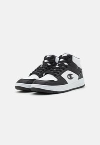 Sneakers bianco e nero con un design in pelle e rete, caratterizzati da una punta rotonda, chiusura con lacci e un logo sul lato. Suola in gomma.