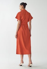 Rust-colored midi dress with a belted waist, short sleeves, and a collared neckline. Smooth fabric, minimalist design, and no visible patterns.
