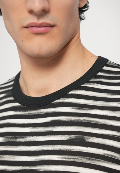 Melns un balts svītrains T-krekls ar apaļu kaklu, kas izceļas ar mīkstu tekstūru un nevienmērīgu otu triepienu rakstu audumā.