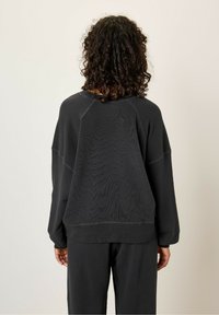 Sweat-shirt noir avec une coupe décontractée, des manches longues et des poignets côtelés. Il présente un tissu texturé et des détails cousus. Assorti à un pantalon coordonné.