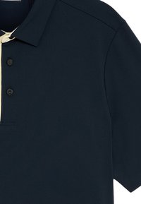 Mörkblå pikétröja med krage, med en ljus krämfärgad placket och två knappar. Slät tyg, korta ärmar, minimalistisk design.